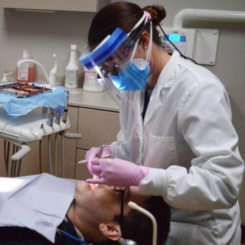 a female dentist treating an adult male patient with glasses